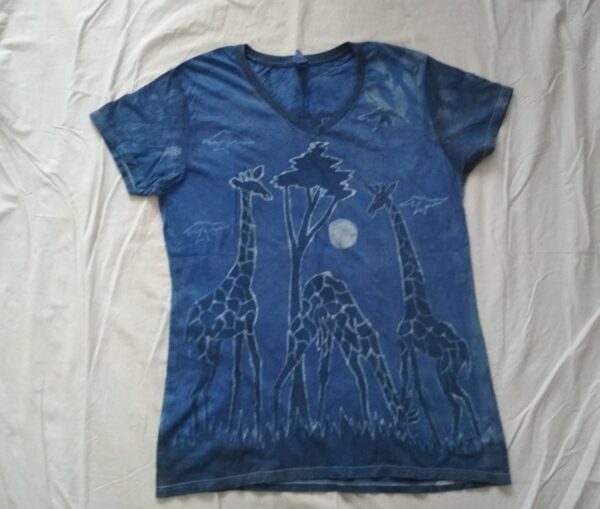 T-shirt batik for women. In front, three giraffes one of which in the middle grazes the grass and in the back two giraffes whose neck is crossed; blue light. 68 x 37 cm.
